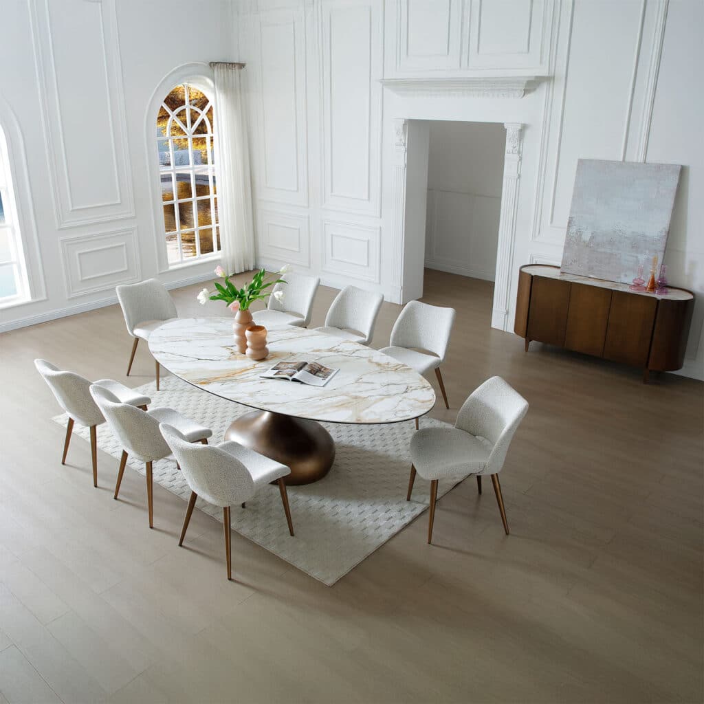 Oval gold-veined ceramic dining table with bronze pedestal base and light grey fabric chairs